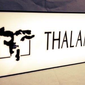 Könnte beinhalten: Ein weißes Schild mit schwarzem Text und einer schwarzen Silhouette eines Gesichts. Der Text lautet "THALAMUS".