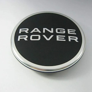 Pode incluir: Um emblema redondo preto e prateado com o texto "RANGE ROVER" em letras brancas.