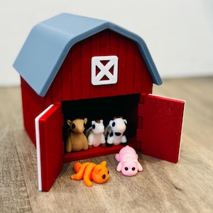 May include: A red barn with a grey roof and white trim, with open red doors revealing miniature farm animals. The barn houses a brown bear, two cows, and a pink pig, with an orange cat lying outside.