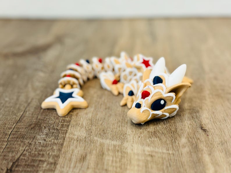 Pu&ograve; includere: Una stravagante statuetta di drago articolata in beige, bianco, rosso e blu. Il corpo del drago &egrave; segmentato, con una coda a forma di stella e una testa dettagliata. Il design presenta una combinazione di colori patriottici, con stelle e strisce.