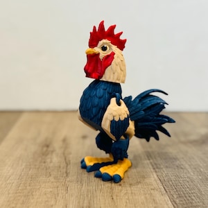 Puede incluir: Figura de gallo colorido con cresta, barbilla y pico rojos. El cuerpo es azul con detalles beige y las patas son amarillas. El gallo está sobre una superficie de madera.