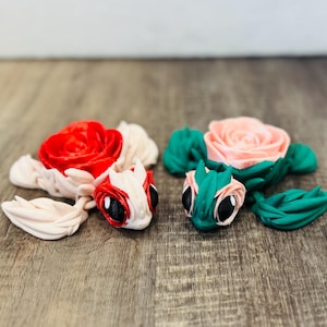 May include: Two whimsical clay turtle figurines. One has a red rose, white petals, and a white and red head with black eyes. The other has a pink rose, green leaves, and a green and white head with black eyes.