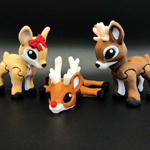 May include: Three brown and white reindeer figurines. One reindeer is lying down with its head turned to the side. The other two reindeer are standing up with their heads turned to the side. The reindeer have black eyes and red noses.
