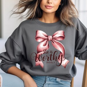 May include: A gray sweatshirt with a pink bow and the text "She is worthy Proverbs 31" printed on the front.