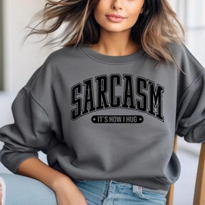 May include: A grey sweatshirt with the text "SARCASM - IT'S HOW I HUG" printed in black.