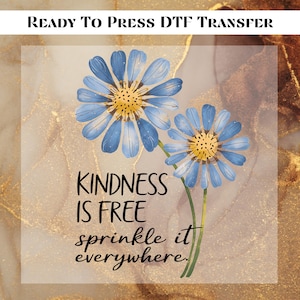 May include: DTF transfer featuring two blue daisy flowers with yellow centers and green stems. The text "KINDNESS IS FREE sprinkle it everywhere" is displayed in black. The background has a gold and white marble effect.