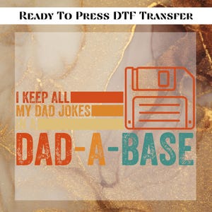 May include: A DTF transfer design with the text "READY TO PRESS DTF TRANSFER". The design features the text "I KEEP ALL MY DAD JOKES" and "DAD-A-BASE" with a floppy disk graphic in orange and teal.
