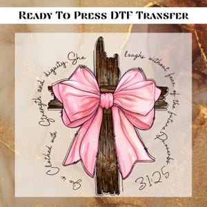 May include: A pink bow tied around a rustic wooden cross with the text "She is clothed with strength and dignity. She laughs without fear of the future. Proverbs 31:25"