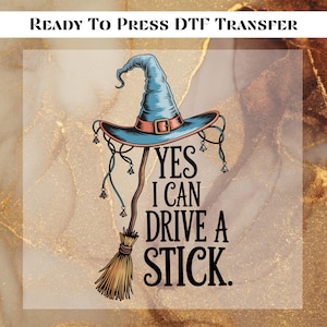 May include: A DTF transfer design featuring a witch's hat and broom with the text "YES I CAN DRIVE A STICK." The hat is blue with a brown brim and buckle. The broom is brown and tan. The background is a gold and brown marble pattern.