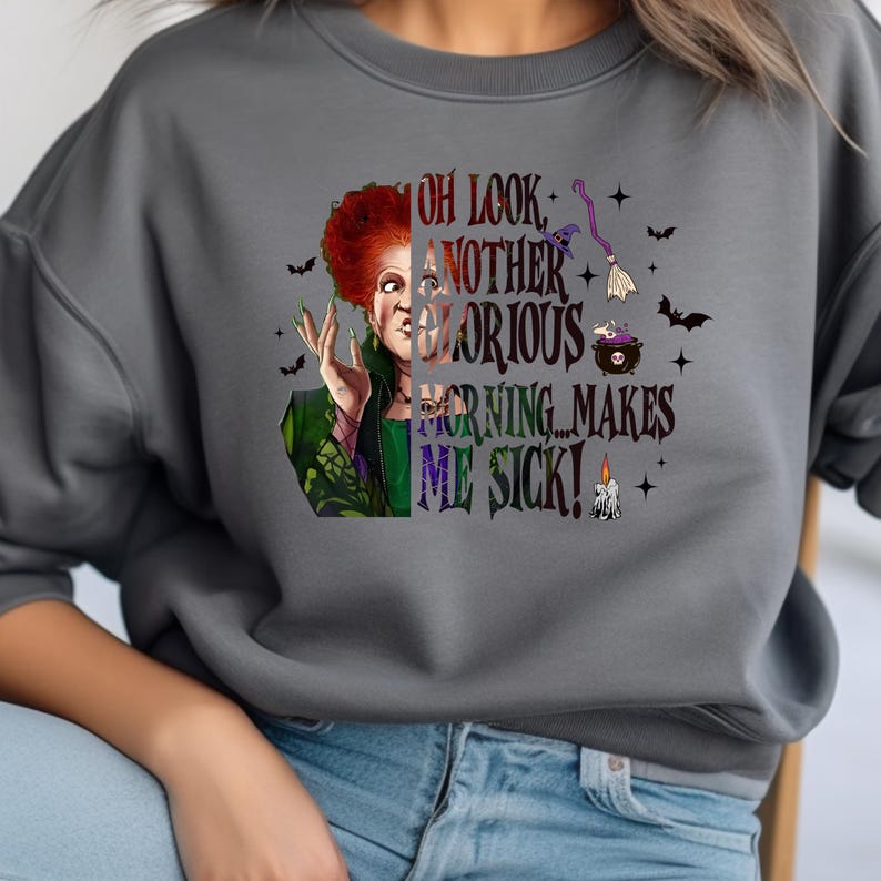 May include: Gray sweatshirt featuring a graphic of a character with red hair and the text "OH LOOK, ANOTHER GLORIOUS MORNING... MAKES ME SICK!" with bats, a witch hat, a cauldron, a broom, and a candle.
