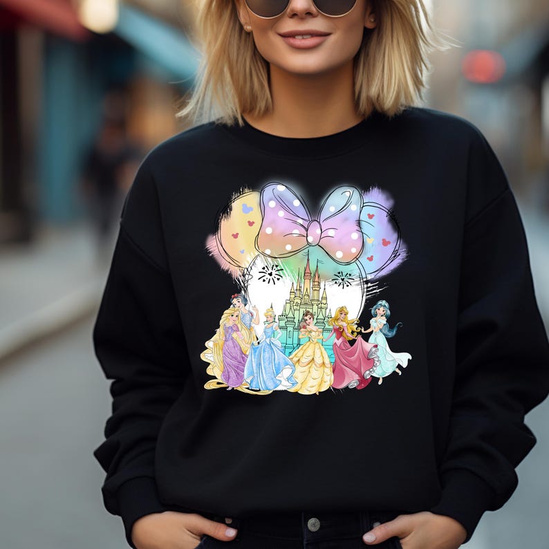 May include: Black sweatshirt with a colorful graphic of Disney princesses and Cinderella's castle in front of a pink bow. The graphic is in the shape of Mickey Mouse ears.