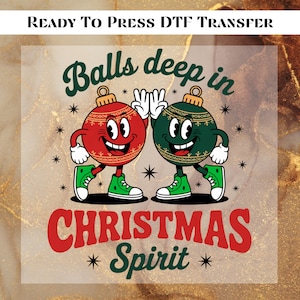 May include: A DTF transfer with a cartoon design featuring two smiling Christmas ornaments. One is red, the other green, both with white gloves and green sneakers. The text reads "Balls deep in Christmas Spirit."