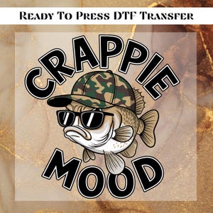 May include: DTF transfer featuring a cartoon crappie fish wearing sunglasses and a camouflage hat. The text "CRAPPIE MOOD" is in bold, black letters with a white outline. The phrase "READY TO PRESS DTF TRANSFER" is at the top.