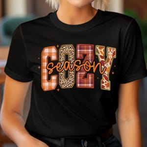 Puede incluir: Camiseta negra con las palabras "COZY SEASON" en un dise&ntilde;o con tem&aacute;tica oto&ntilde;al. Las letras est&aacute;n rellenas de cuadros, estampado de leopardo y hojas de oto&ntilde;o. La palabra "season" est&aacute; en cursiva, con peque&ntilde;os acentos de estrellas.