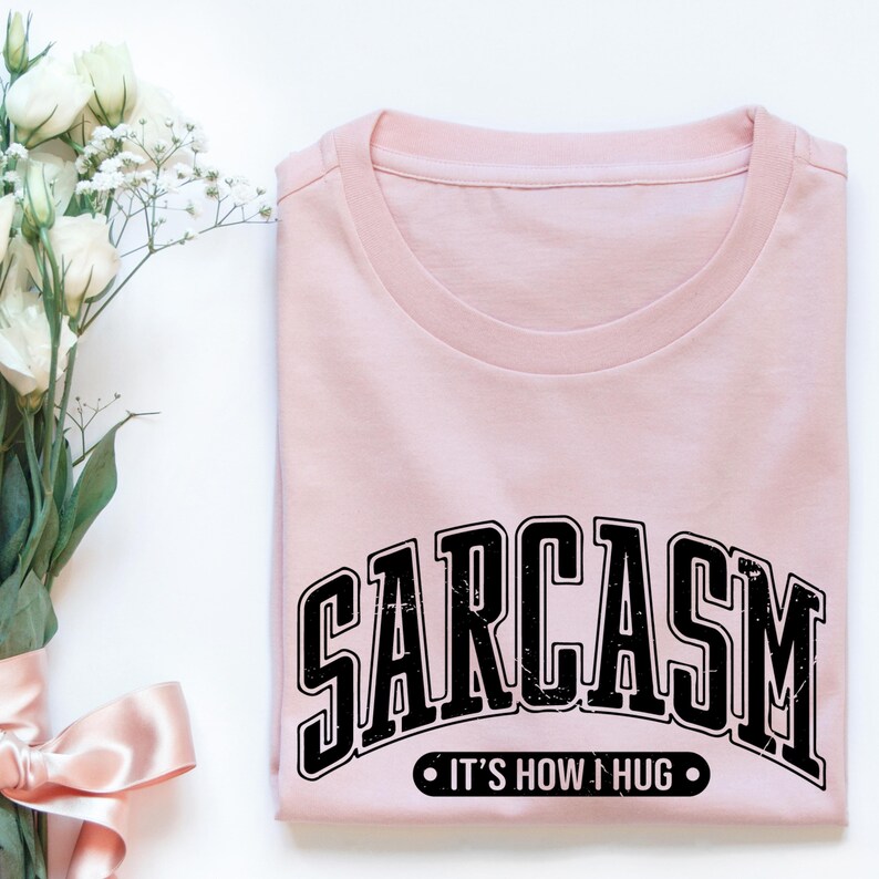 May include: A pink t-shirt with black text that reads "SARCASM IT'S HOW I HUG".