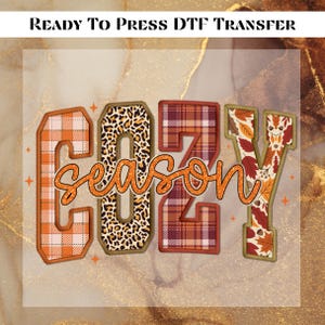 May include: A DTF transfer design with the words "COZY SEASON" in a fall-themed font. The letters are filled with plaid, leopard print, and autumn leaf patterns. The text "READY TO PRESS DTF TRANSFER" is at the top.