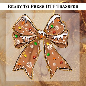 May include: A brown gingerbread bow design with white icing, colorful candies, and gold glitter accents. The bow features snowflake and star details. The text "READY TO PRESS DTF TRANSFER" is at the top.