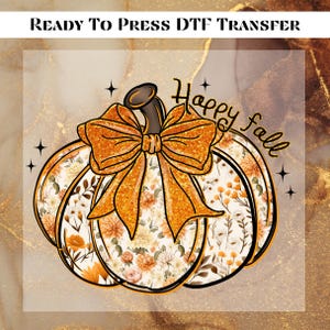 May include: DTF transfer featuring a pumpkin design with a large orange glitter bow and floral pattern. The words "Happy Fall" are written in a script font. Black star accents surround the pumpkin. The words "READY TO PRESS DTF TRANSFER" are at the top.