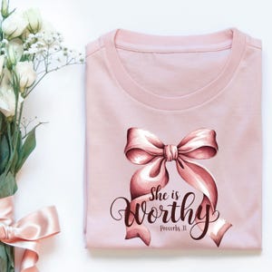 May include: Pink t-shirt with a pink bow and the text "She is worthy Proverbs 31" printed on it.
