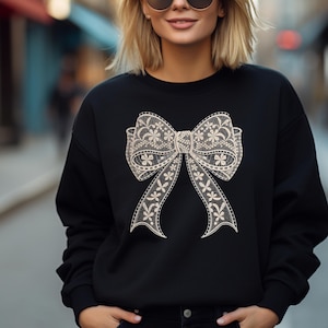 May include: Black sweatshirt with a large white lace bow design on the front.