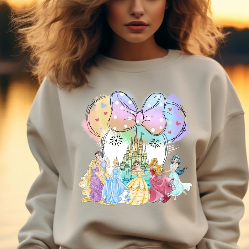 May include: A light gray sweatshirt with a colorful graphic of Disney princesses, Cinderella's castle, and a Minnie Mouse bow.