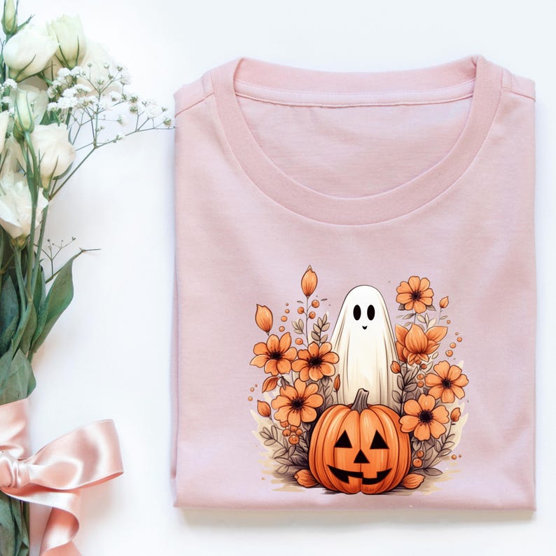 May include: A pink t-shirt with a white ghost and an orange pumpkin with a jack-o'-lantern face in a field of orange flowers.