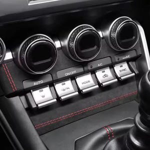 Può includere: Primo piano del cruscotto di un'auto con manopole e pulsanti per il controllo del clima. Il cruscotto nero presenta dettagli argentati e cuciture rosse. Pulsanti: "AUTO", "ON/OFF", "A/C", "MODE" e "SYNC".