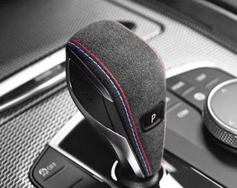 May include: Close-up of a black leather car gear shifter with red and blue stitching. The shifter has a "Park" (P) indicator and the word "Unlock" is visible.