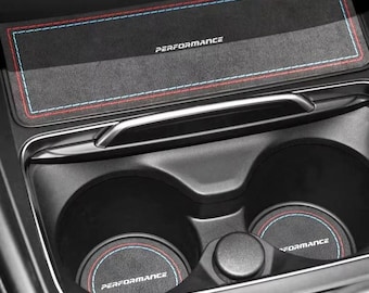 May include: Black car interior accessories, including a rectangular mat and two circular coasters. The mat and coasters have red and blue stitching and the word "PERFORMANCE" printed on them. The accessories are designed to fit in a car's center console.
