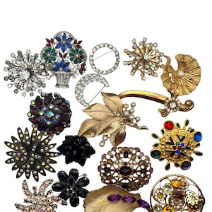 May include: A collection of vintage brooches in various shapes and colors. The brooches include floral, starburst, and geometric designs, with rhinestones, pearls, and other embellishments. Some are silver-toned, gold-toned, and black.