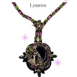 May include: A necklace with purple, green, and gold accents, featuring the text "Alice Caviness Purple. Onyx & Green Necklace with Gold Filigree Leaves." It has a black onyx pendant with gold filigree leaves, and is decorated with purple and green gemstones.