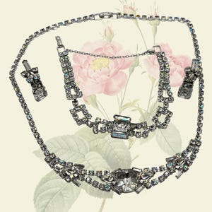 Puede incluir: Juego de joyas vintage de pedrería helada, que incluye un collar, una pulsera y pendientes. El conjunto presenta brillantes pedrerías transparentes engastadas en metal plateado. El texto en la parte superior dice "VINTAGE ICY RHINESTONE D'VERS JEWELRY SET".