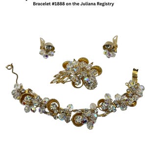 May include: A vintage Juliana Demi Parure metal cup jewelry set, including a bracelet, earrings, and a brooch. The set features clear crystal stones and gold-tone metal. The bracelet is bracelet #1888 on the Juliana Registry. Text on the image reads: "Verified Juliana Demi Parure Metal Cup Jewelry Set - Book Piece".