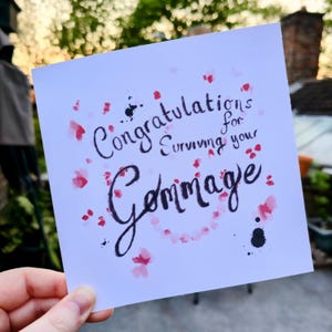 May include: A white card with black ink calligraphy that reads "Congratulations for surviving your Gemmage." The card is decorated with pink watercolour splatters.