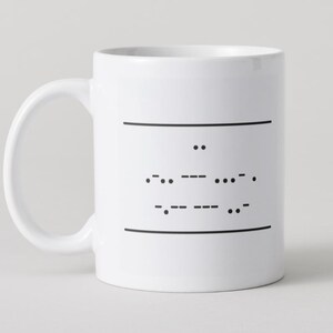 May include: White ceramic mug with a curved handle. The mug features a black Morse code design between two horizontal black lines. The Morse code spells out a message. The mug is a standard size for tea or coffee.