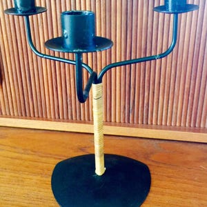 May include: Black metal candle holder with three arms and a woven base. The holder has a heart-shaped base.