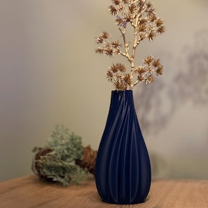 May include: A dark blue vase with a textured, ribbed design holds a dried branch with small, golden brown flower buds.