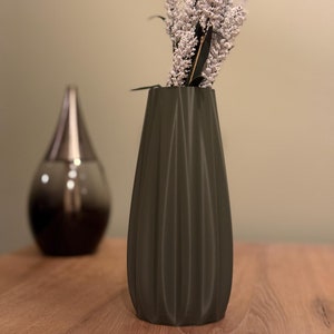 Op de afbeelding: Een donkergroene keramische vaas met een geribbeld ontwerp, met een boeket witte bloemen.