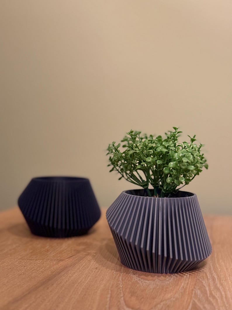 May include: Two grey geometric planters, one with a small green plant. The planters have a ribbed design and are on a wooden surface.