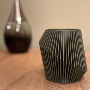 May include: A dark grey geometric planter with a ribbed design. The planter is made of a smooth, matt material and has a slightly rounded base.