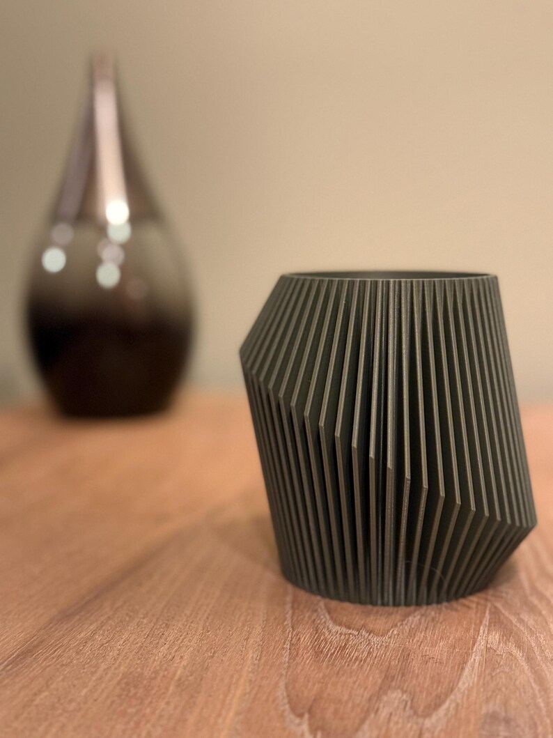 May include: A dark grey geometric planter with a ribbed design. The planter is made of a smooth, matt material and has a slightly rounded base.