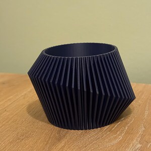 May include: A dark blue, geometric planter with a ribbed design. The planter is made of a smooth, hard plastic and has a wide, round opening.