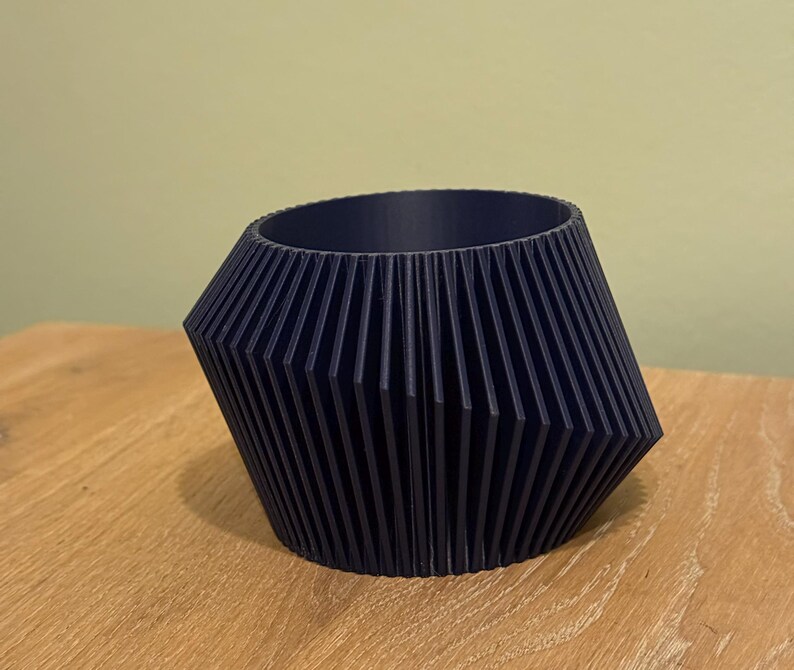 May include: A dark blue, geometric planter with a ribbed design. The planter is made of a smooth, hard plastic and has a wide, round opening.