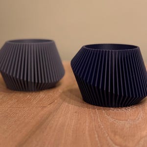 May include: Two dark blue, geometrically shaped planters with a ribbed design. The planters are made of a smooth, matte material.