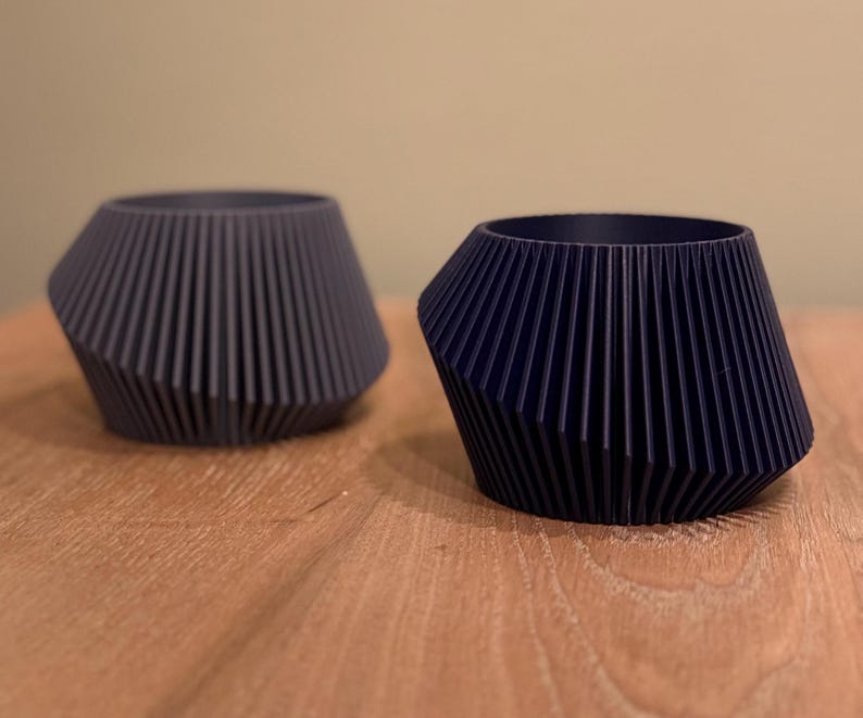 May include: Two dark blue, geometrically shaped planters with a ribbed design. The planters are made of a smooth, matte material.