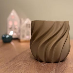Op de afbeelding: Een bruine keramische plantenpot met een draaiende, textuur. De pot is leeg en heeft een gladde, ronde bodem.