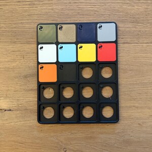 May include: A black colour chart with 18 colour swatches, including green, brown, blue, grey, white, light blue, yellow, red, orange, and black. The chart also has 9 empty circles.