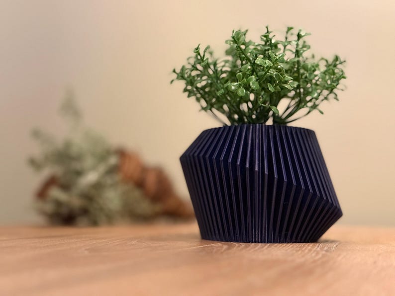 May include: A dark blue, geometric planter with a ribbed design, holding a small green plant.