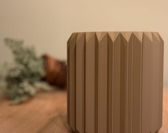 May include: A brown, cylindrical planter with a geometric, ribbed design. The planter is made of a smooth, matte material.