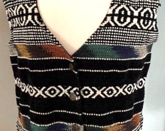 May include: A black, button-down vest with a V-neck, featuring a geometric pattern in white and colorful horizontal stripes. The vest is sleeveless and appears to be made of a woven fabric.